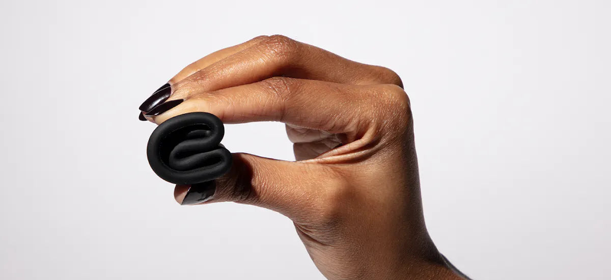 Hand holding a folded menstrual cup in punch-down fold position against a plain background