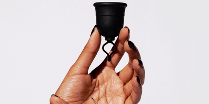 Hand holding a menstrual cup by the stem against a plain background