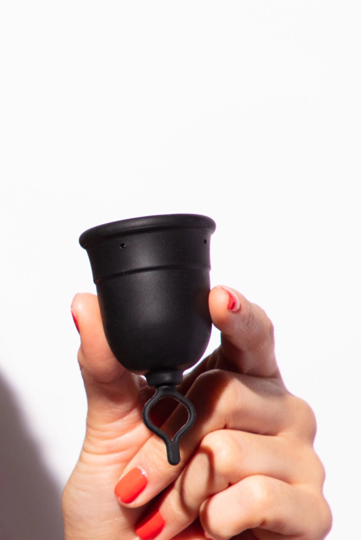 Hand holding a menstrual cup with a looped stem against a white background